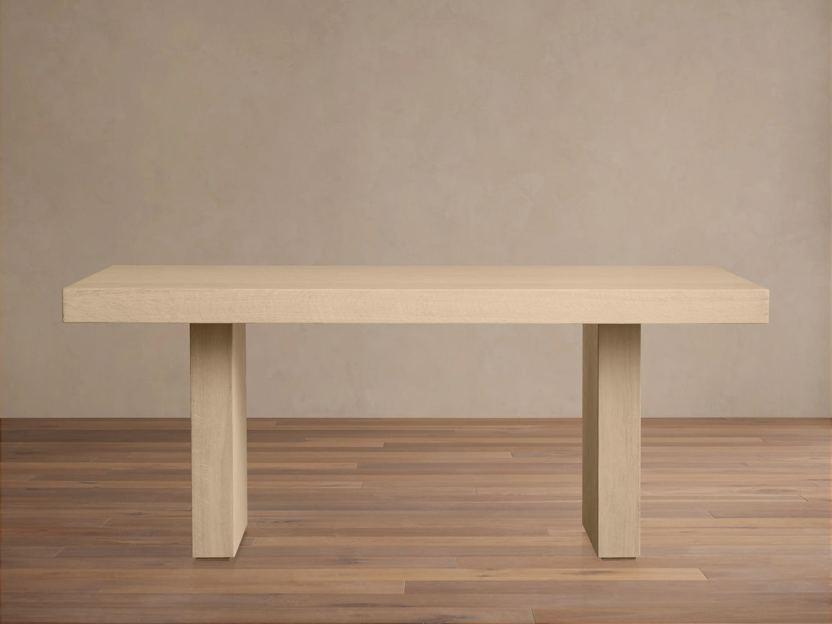 Calvin Dining Table: light oak rectangular table with two thick pedestal legs, natural wood grain, centered on wood floor.