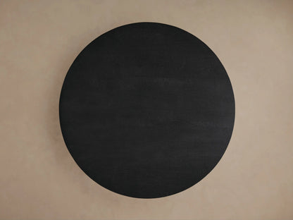 Calderone Dining Table: Angled close-up of a round sandblasted black mango wood top, thick curved & angular base.