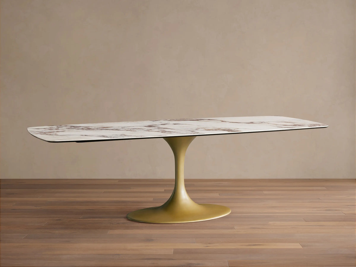 Ceramic Vincenza Dining Table with calacatta marble design and a golden steel base, set on a wooden floor against a beige wall.