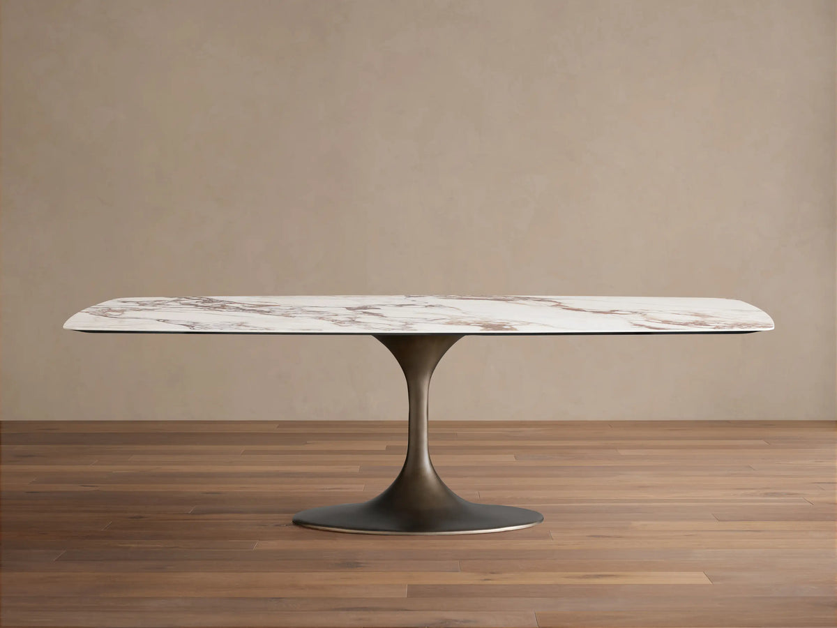Vincenza Dining Table with Launette Base, ceramic top with calacatta marble design, steel base, on wooden floor.