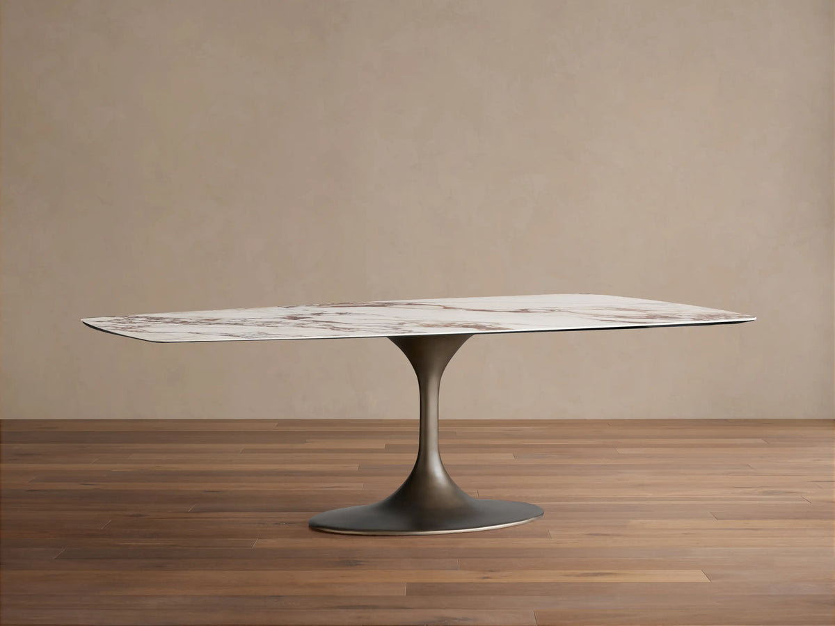 Vincenza Dining Table with Launette Base, ceramic top with calacatta marble design, steel base, on wooden floor.
