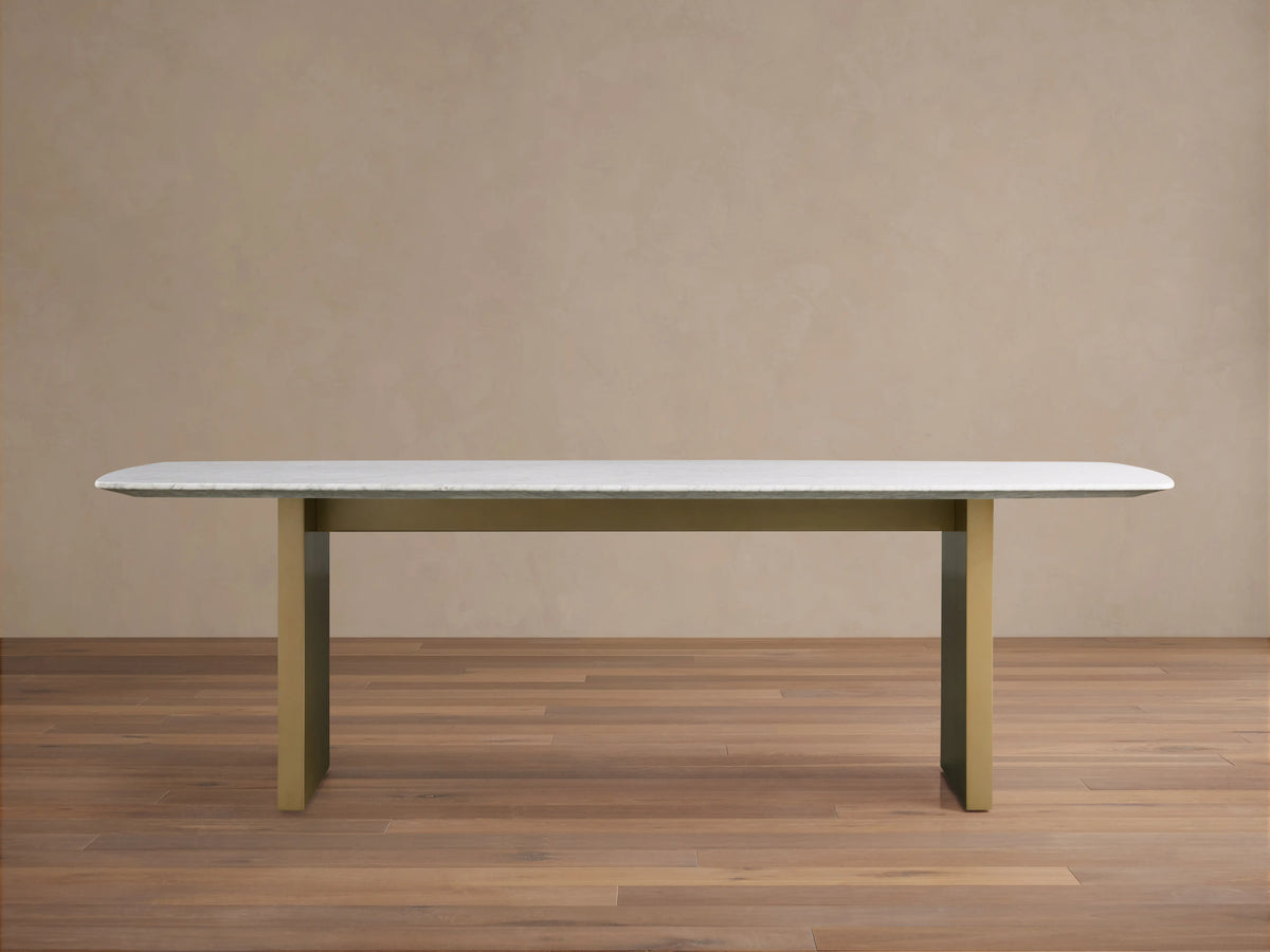 Saint Germain Stone Dining Table with white marble top and olive brown base on wood floor, minimalistic setting.