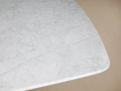 Saint Germain Stone Dining Table with a long, white Carrara marble top and a rectangular, bronze-colored Clement base on a wood floor.