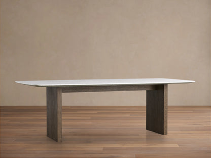 Saint Germain dining table with a Carrara marble top and two thick wood legs in a chestnut finish on a wooden floor.