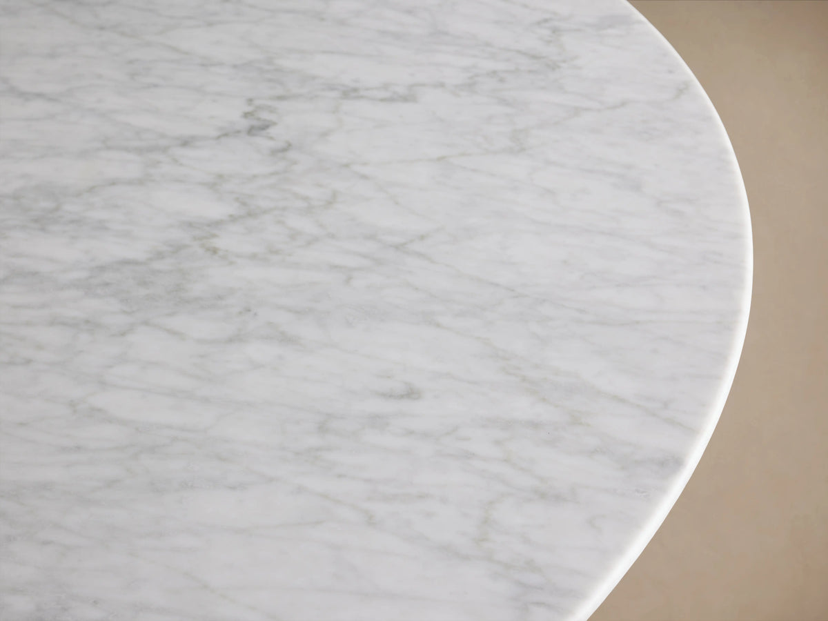 Close-up of the Saint Germain Round Stone Dining Table's white Carrara marble top with subtle gray veining, showing a curved edge.