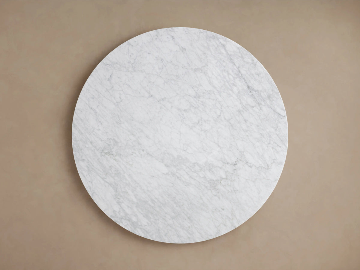Round dining table with a white Carrara marble top and a gold-toned steel base, set against a neutral background.