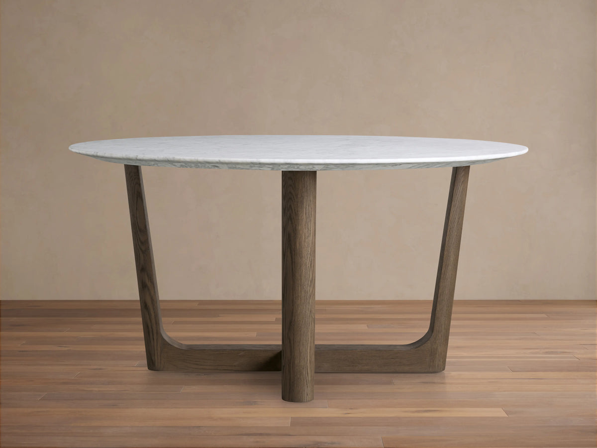 Saint Germain round dining table with white marble top and dark wood Rennes base on a wooden floor, against a beige wall.