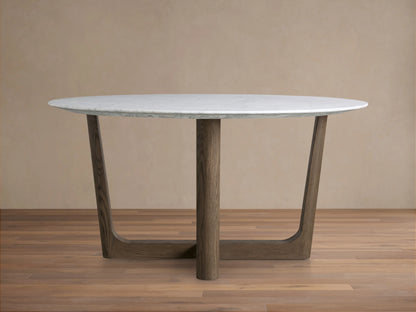 Saint Germain round dining table with white marble top and dark wood Rennes base on a wooden floor, against a beige wall.