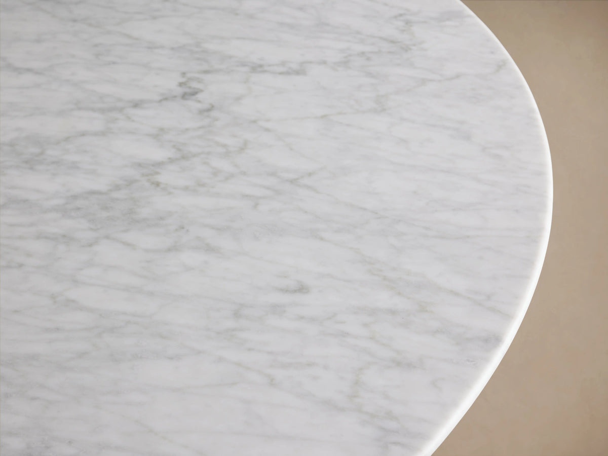 Saint Germain Round Stone Dining Table with a Carrara marble top on a U-shaped Rennes base made of oak wood, indoors on wooden floor.