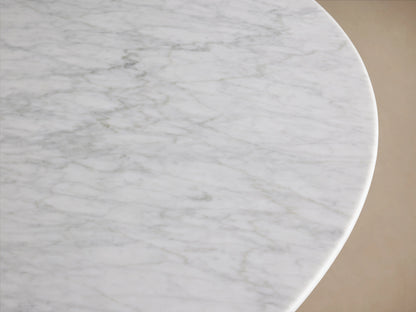 Saint Germain Round Stone Dining Table with a Carrara marble top on a U-shaped Rennes base made of oak wood, indoors on wooden floor.