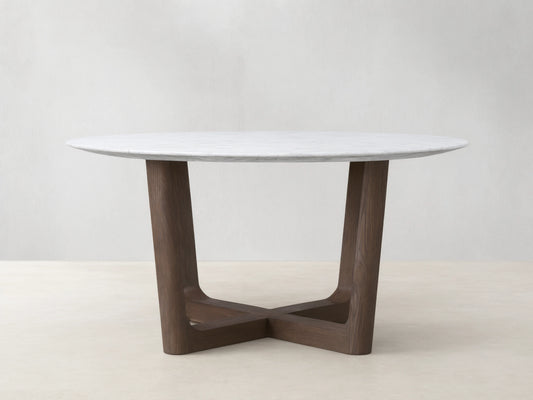 Saint Germain round dining table with white marble top and dark wood Rennes base on a wooden floor, against a beige wall.