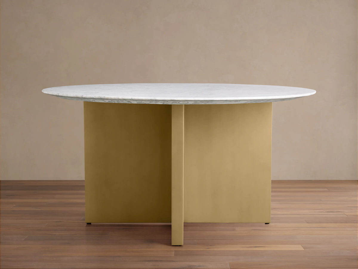 Saint Germain round dining table with a white Carrara marble top and V-shaped antique brass steel base on a wooden floor.
