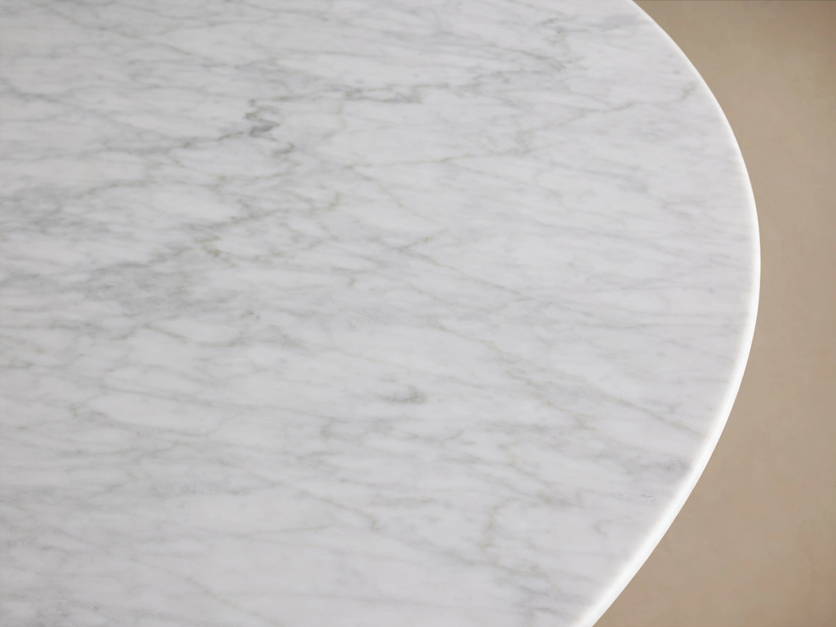Saint Germain dining table with a round light stone top and a dark wood base on a wooden floor, against a beige wall.