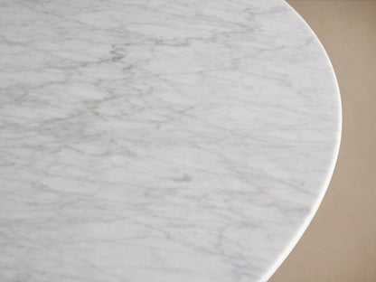 Saint Germain dining table with a round light stone top and a dark wood base on a wooden floor, against a beige wall.