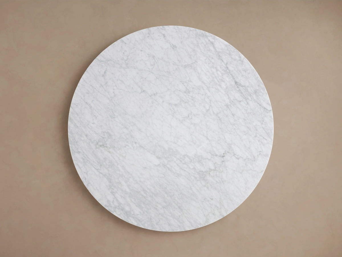 Round Carrara marble tabletop with visible veining patterns in light grey and white tones, showcasing smooth, polished surface.