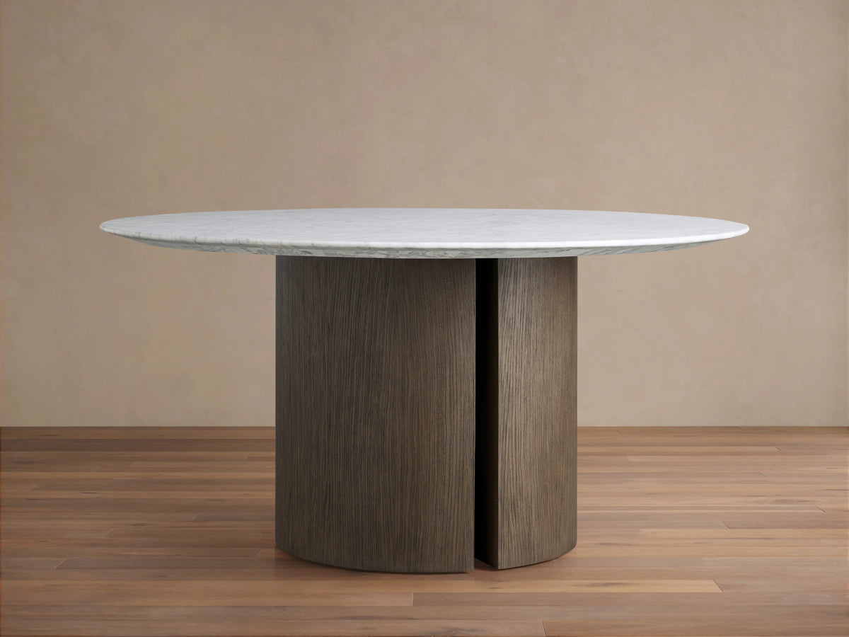 Round dining table with a white Carrara marble top and a sturdy brown oak veneered base. The marble surface shows subtle veining.