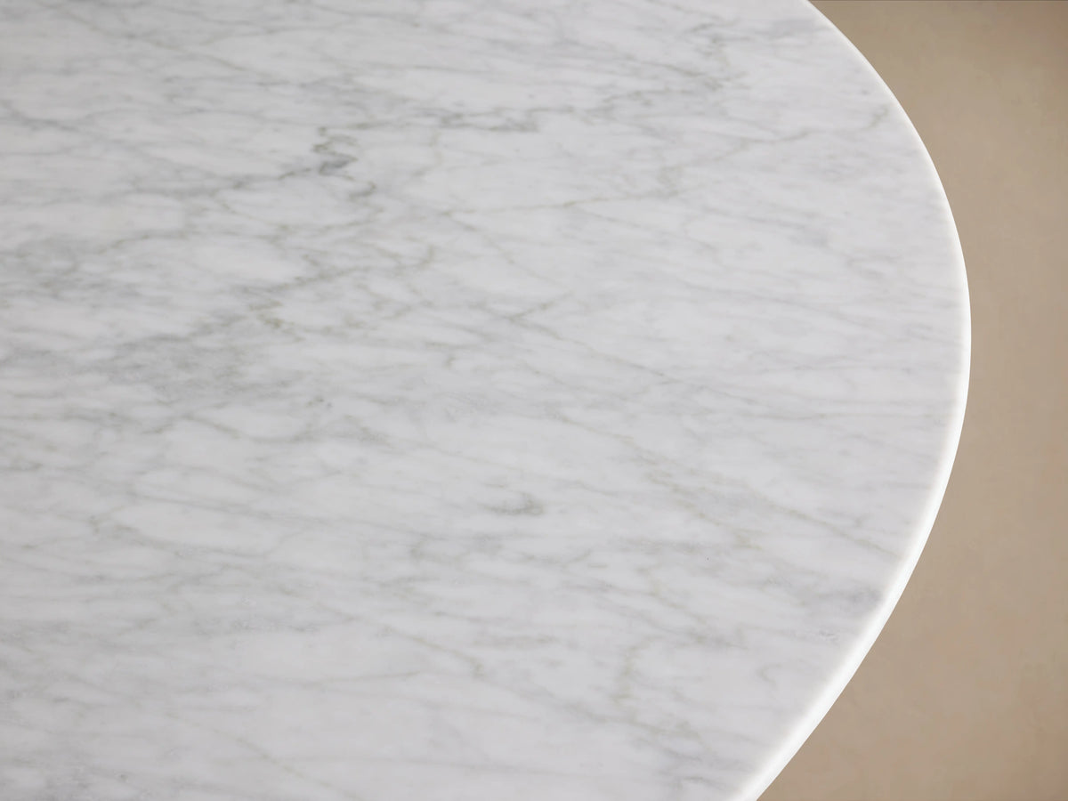 Round dining table with a white Carrara marble top and a sturdy wood base in chestnut finish, placed on a wooden floor.
