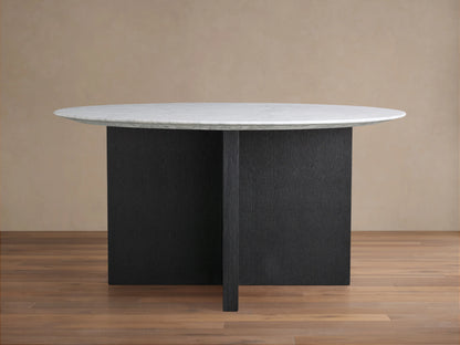 Round dining table with white Carrara marble top and dark wood base on brown wooden floor, beige wall background.
