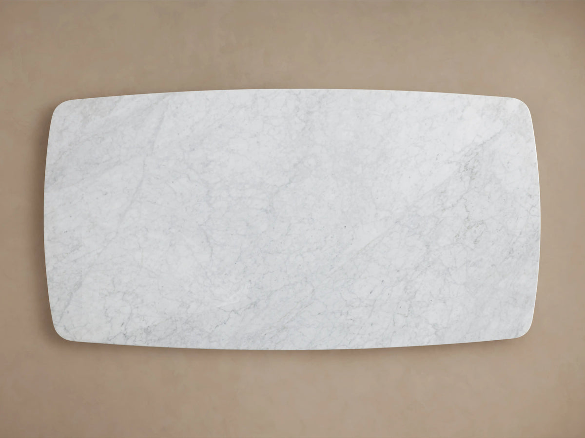 Close-up of the Saint Germain Dining Table's Carrara marble top, showing light gray veining against a white background, with rounded edges.
