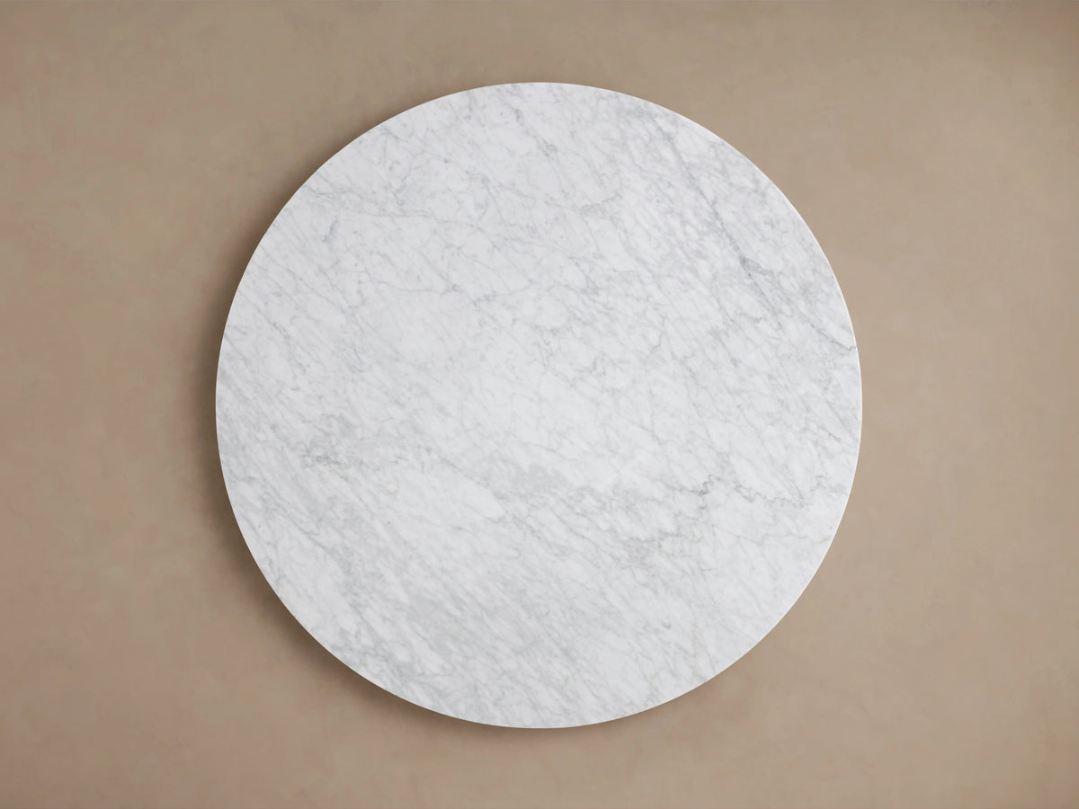 Round dining tabletop made of white Carrara marble, visible gray veining, smooth polished surface, on neutral background.