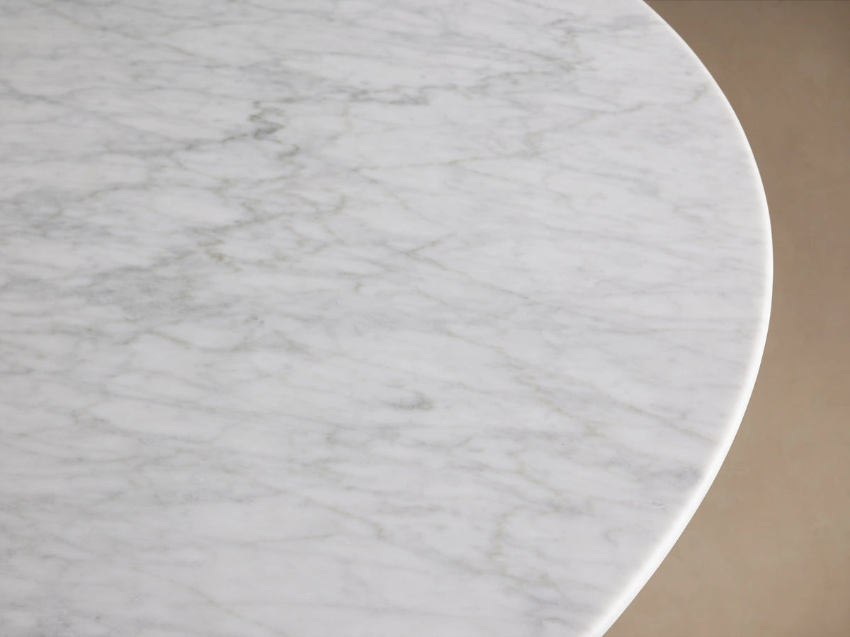 Saint Germain round dining table with a white Carrara marble top and dark steel launette base on a wooden floor.