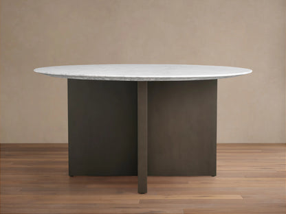 Round dining table with a white Carrara marble top and a V-shaped dark brown base on a wooden floor against a beige wall.