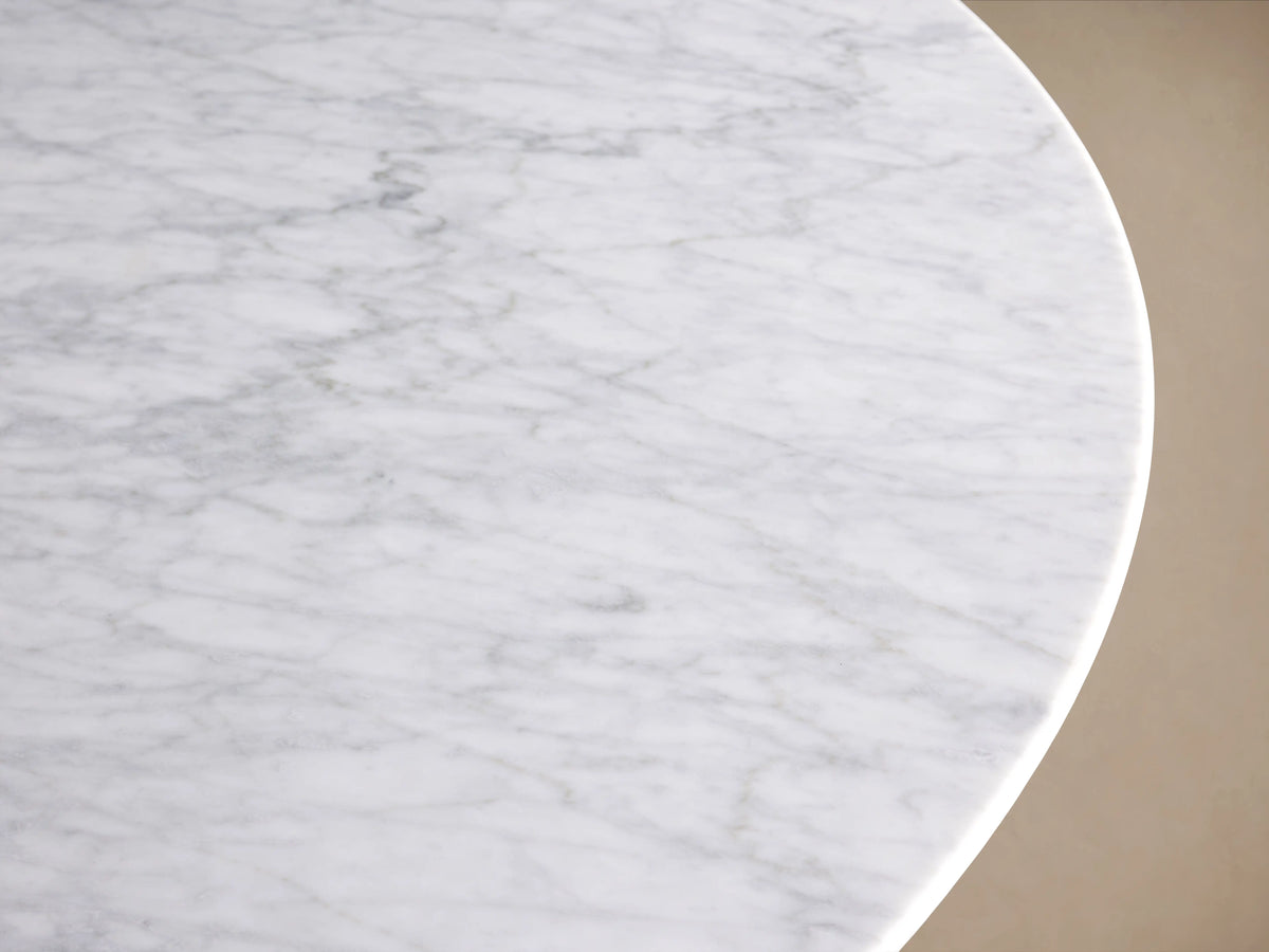 Round dining table with a smooth white stone top, set on a wide, dark rectangular base, resting on wood flooring.