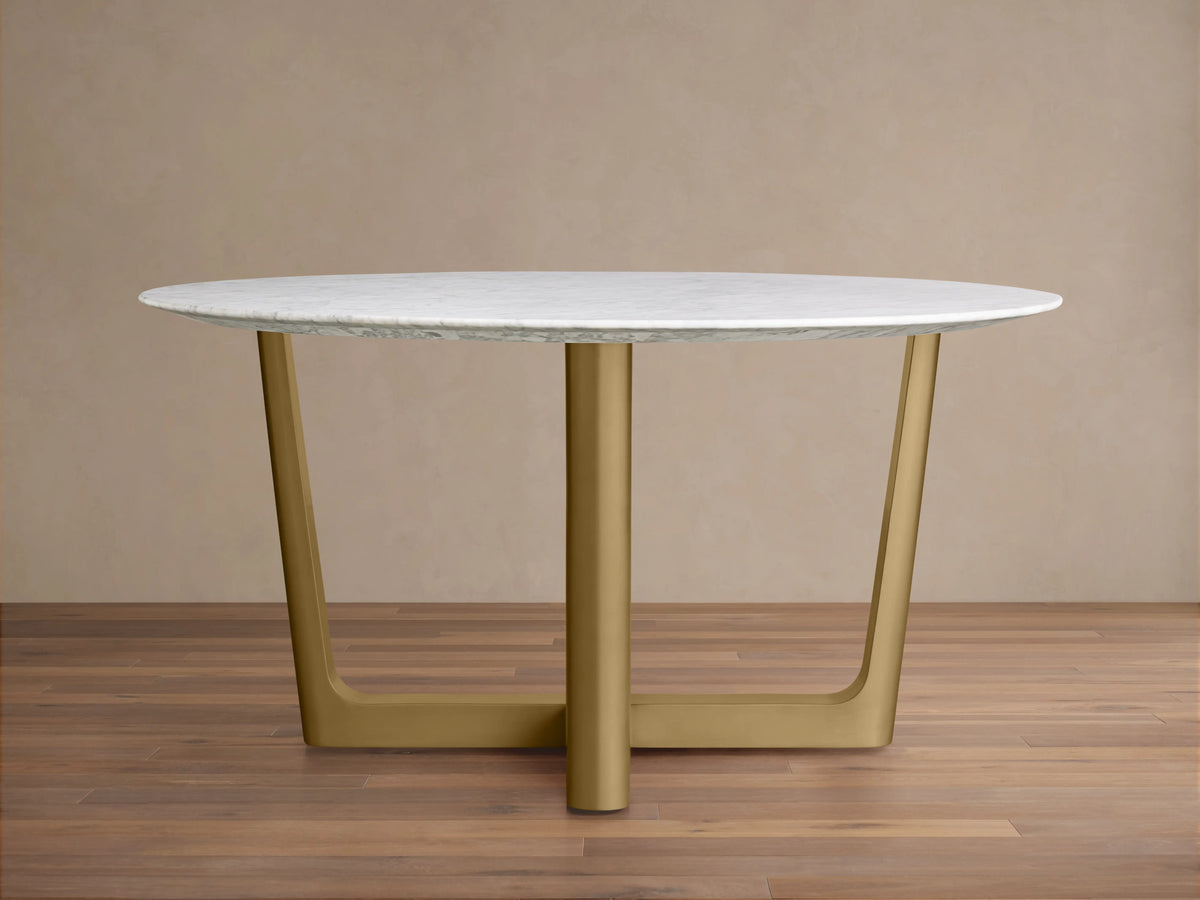 Saint Germain Round Stone Dining Table with a Carrara marble top and a Rennes base in chestnut finish, placed on a wooden floor.