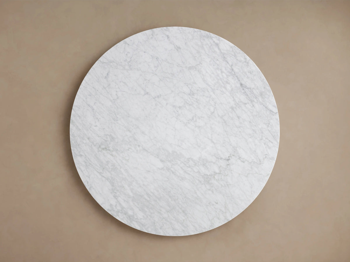 Round Carrara marble tabletop with subtle gray veining on a smooth surface, showing natural variations and edges.