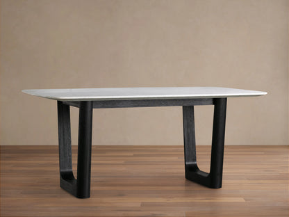 A rectangular dining table with a white Carrara marble top and a thick black wooden base, set on a wooden floor with a beige wall background.