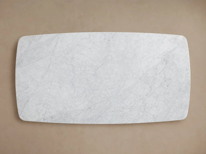 Saint Germain Stone Dining Table with a rectangular Carrara marble top, featuring a unique pattern. It has a dark wood Rennes base in an arch shape, on a wooden floor.