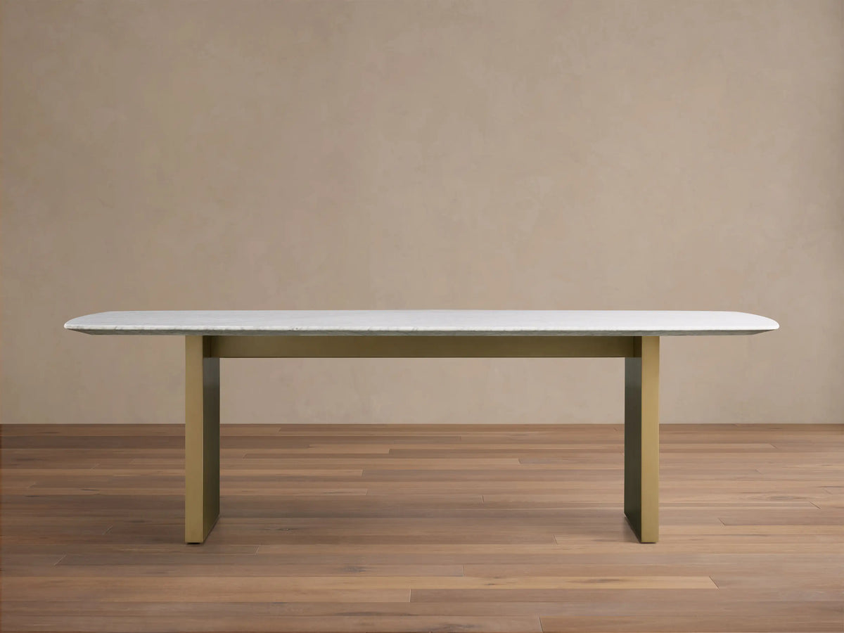 Front view of the Saint Germain 96" Stone Dining Table with Metal Clement Base, white stone top and brass bases.