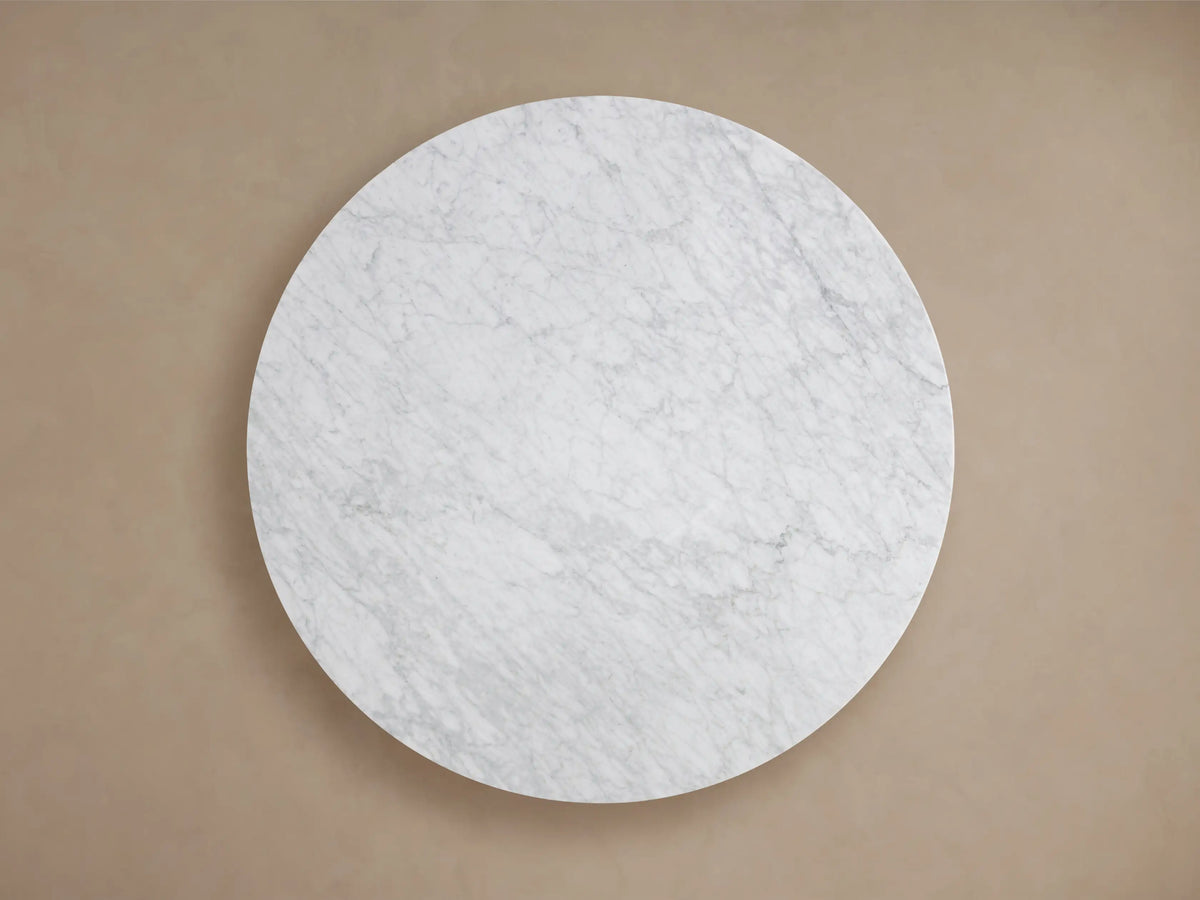 Round stone dining table with a Carrara marble top, featuring natural gray veining patterns, shown in close-up.