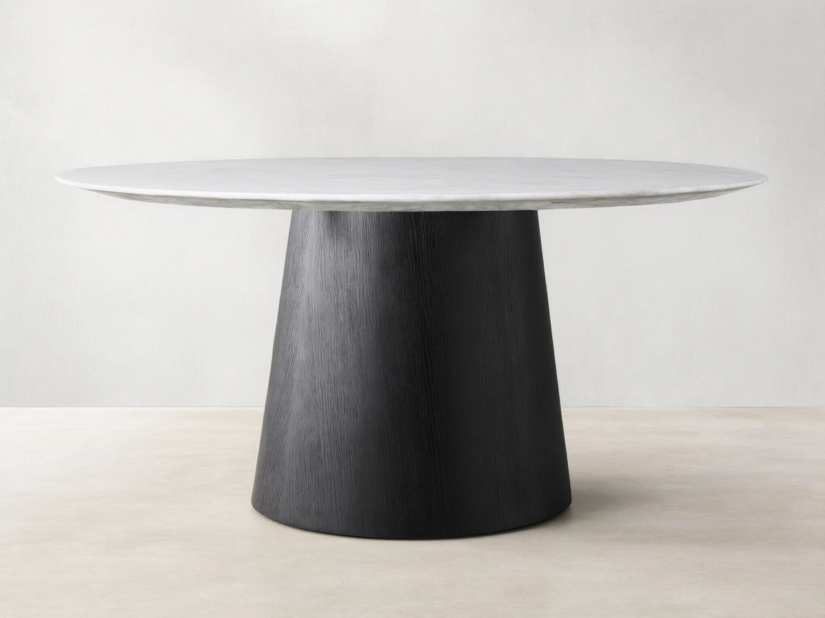 Round dining table with a Carrara marble top in white, featuring subtle veining. The base is a black, cone-shaped structure made of plywood and oak veneers.
