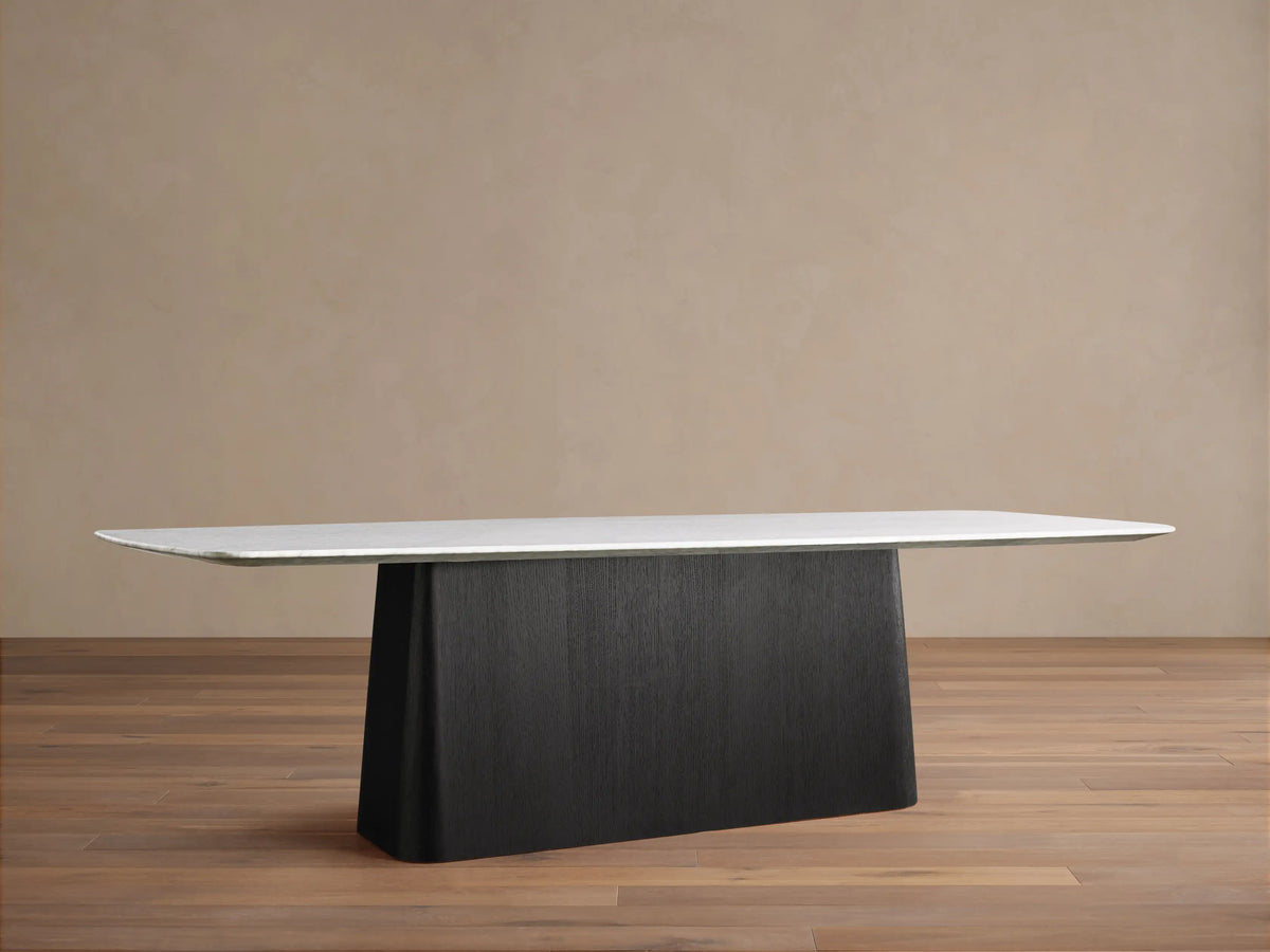 Saint Germain dining table, white Carrara marble top with rounded edges, dark espresso wood base, in a room with wood floor.