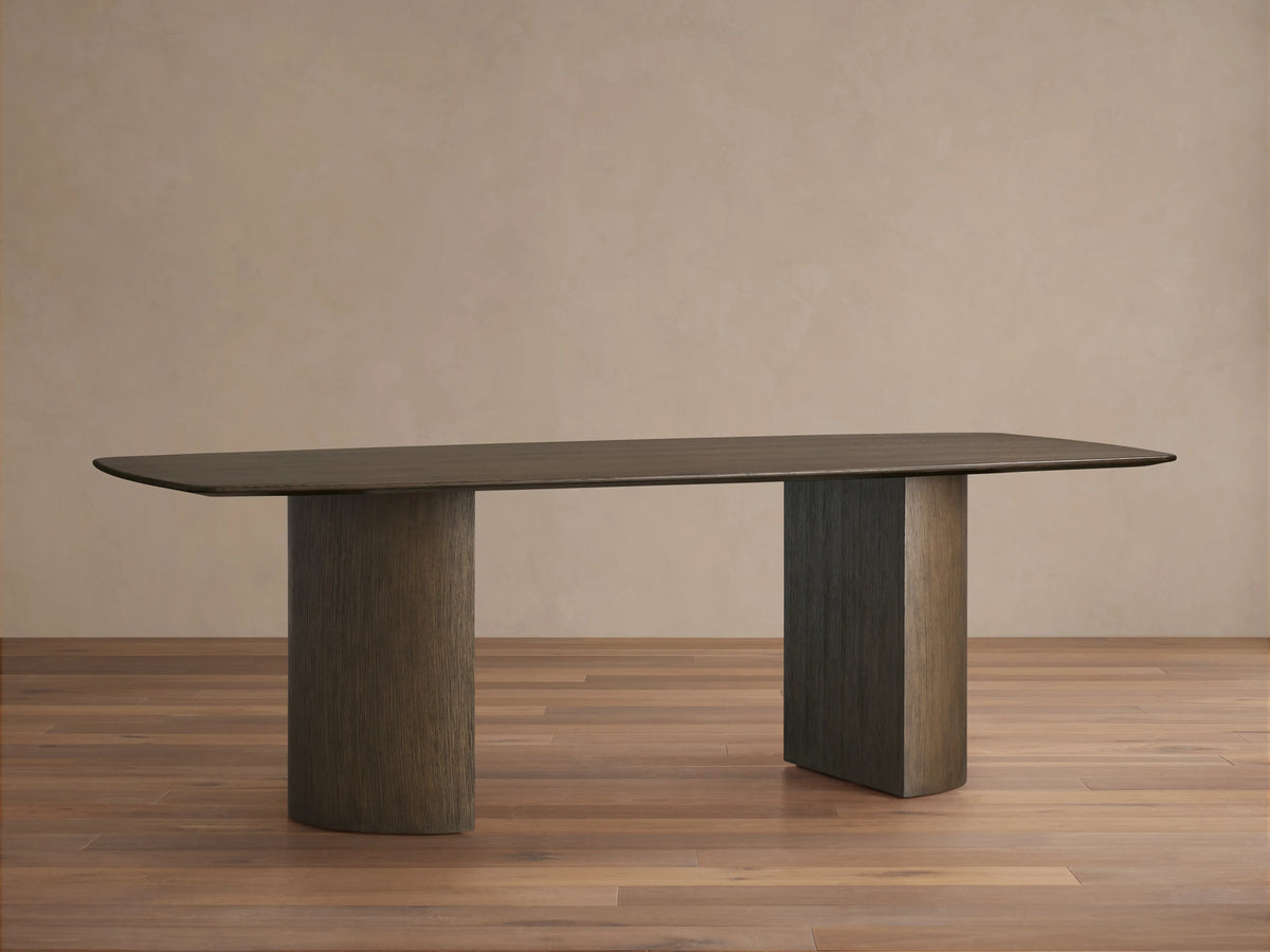 Saint Germain Wood Dining Table with an oval tabletop in a dark finish on two cylindrical bases on a wooden floor.