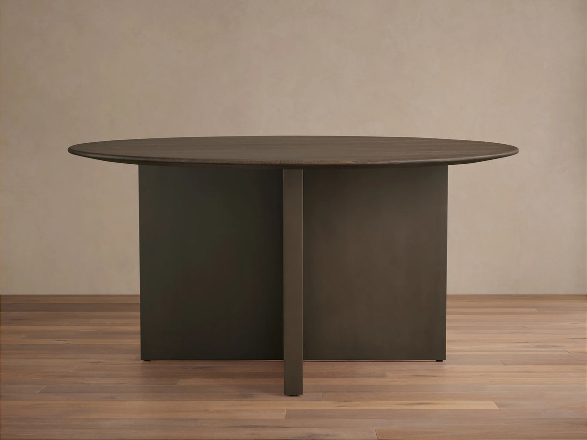 Saint Germain Round Wood Dining Table with Chestnut-finished oak top and dark geometric base, set on wooden floor.