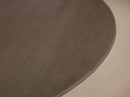 Saint Germain round dining table with a flat wood top and thick ebony-finished base, set on a wooden floor against a beige wall.