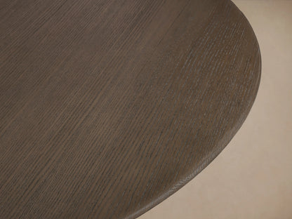 Saint Germain round dining table with a solid oak top in Ebony, featuring a geometric, cross-shaped wood base on a wooden floor.