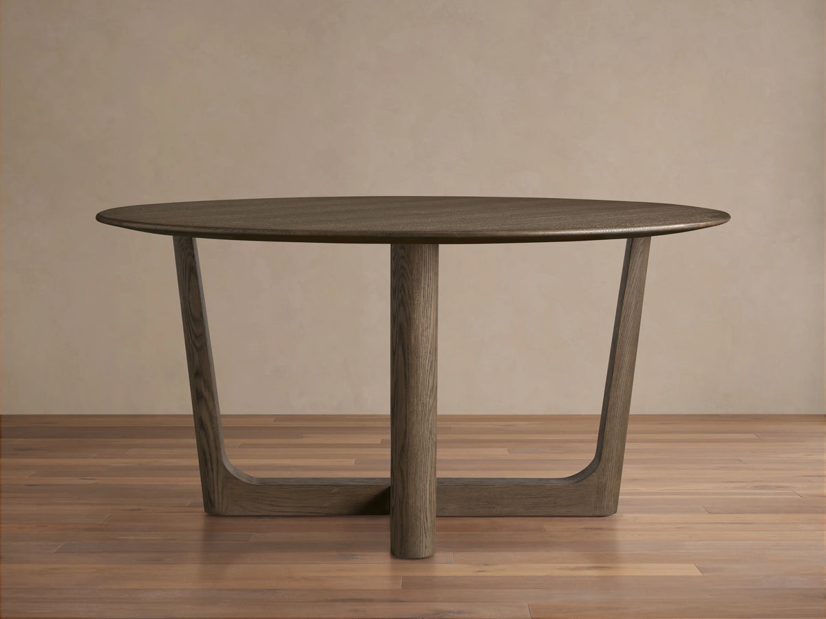 Round wood dining table with solid oak tabletop and Rennes base in dark brown finish, placed on wooden floor against beige wall.
