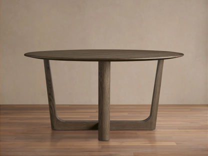 Round wood dining table with solid oak tabletop and Rennes base in dark brown finish, placed on wooden floor against beige wall.