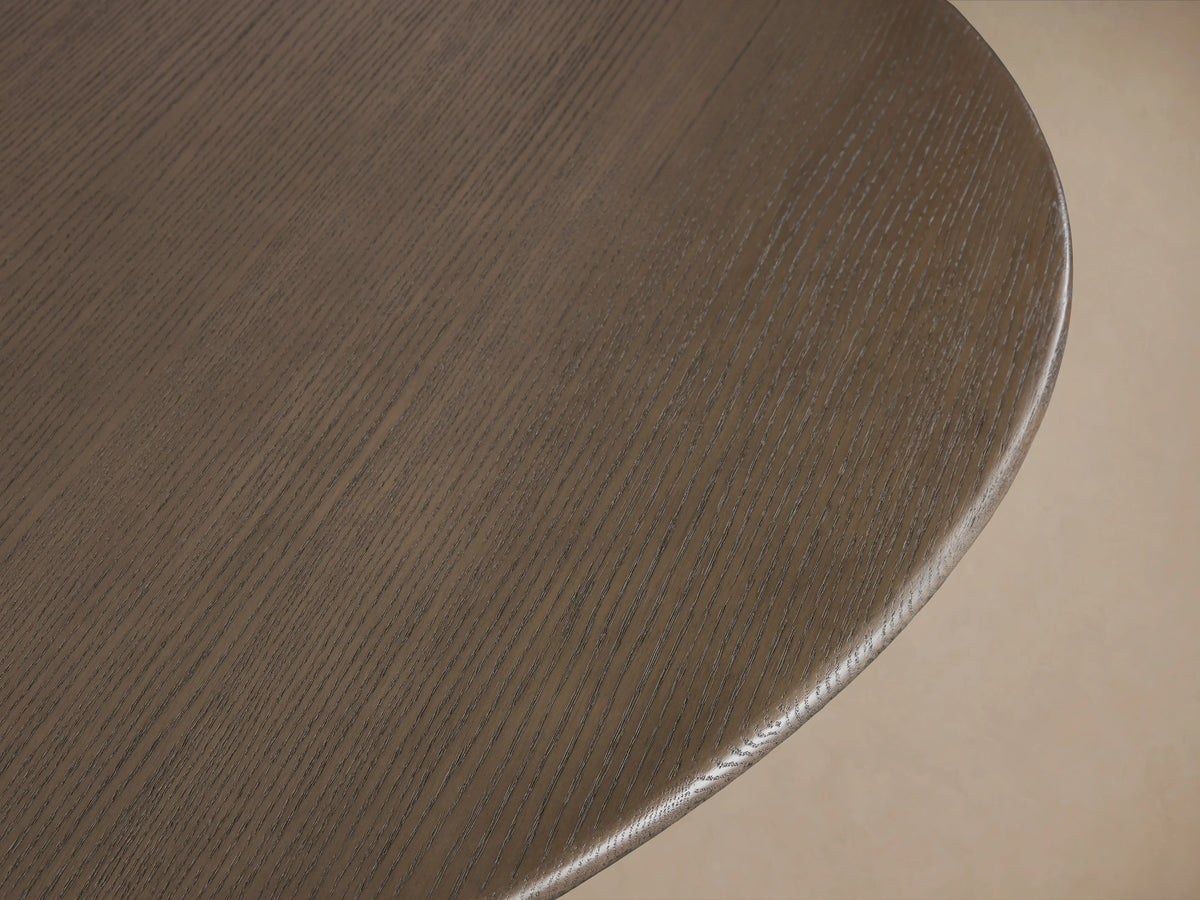 Saint Germain round dining table with a smooth oak tabletop and curved Rennes base, finished in a rich wood tone, on wooden floor.