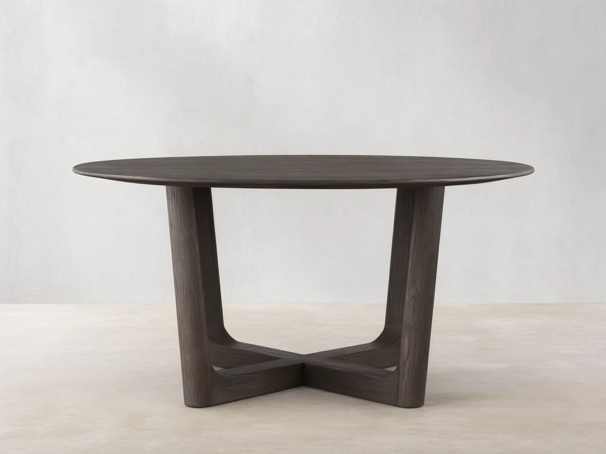 Round wood dining table with solid oak tabletop and Rennes base in dark brown finish, placed on wooden floor against beige wall.