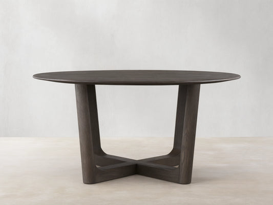 Round wood dining table with solid oak tabletop and Rennes base in dark brown finish, placed on wooden floor against beige wall.