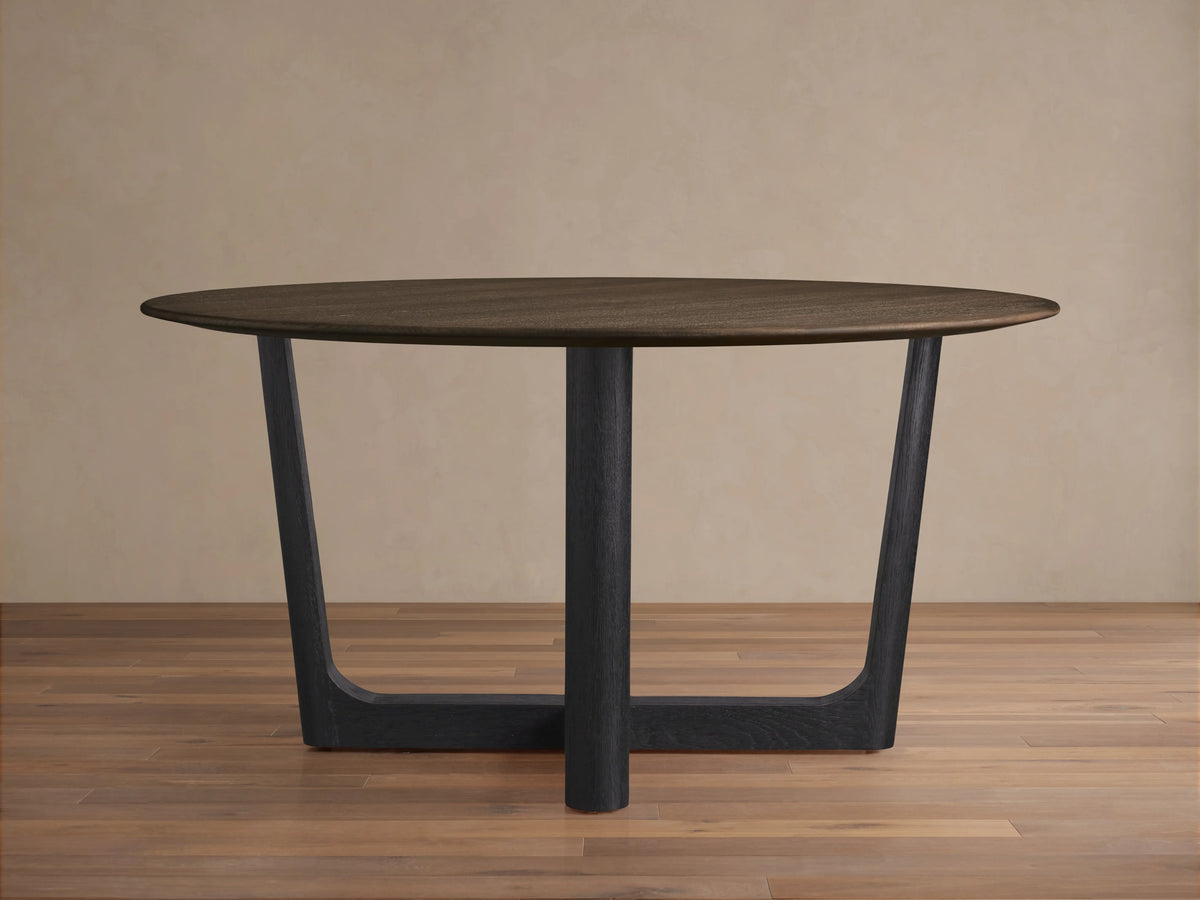 Saint Germain Round Wood Dining Table with a dark brown oak tabletop and an ebony-finished base on a wooden floor.