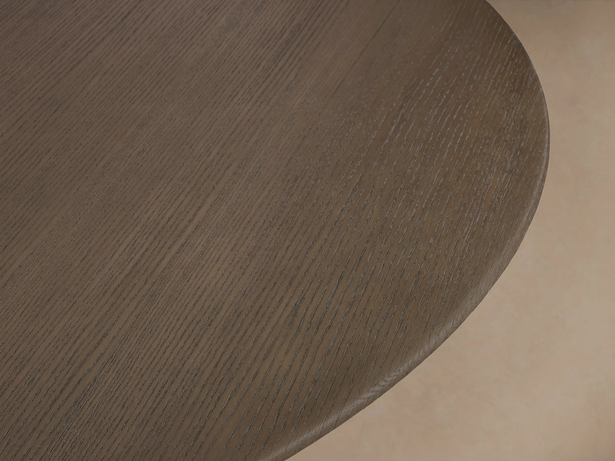Round dining table with a chestnut-finished oak top and a sturdy, antique bronze metal base on a wooden floor.