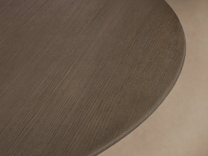 Round dining table with a chestnut-finished oak top and a sturdy, antique bronze metal base on a wooden floor.