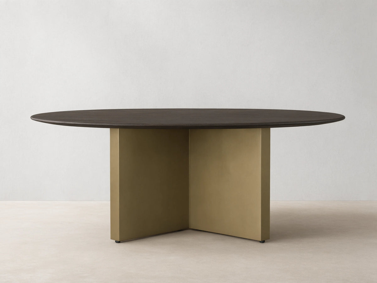 Round dining table with a solid oak chestnut finish top and a V-shaped antique brass steel base on a wooden floor.