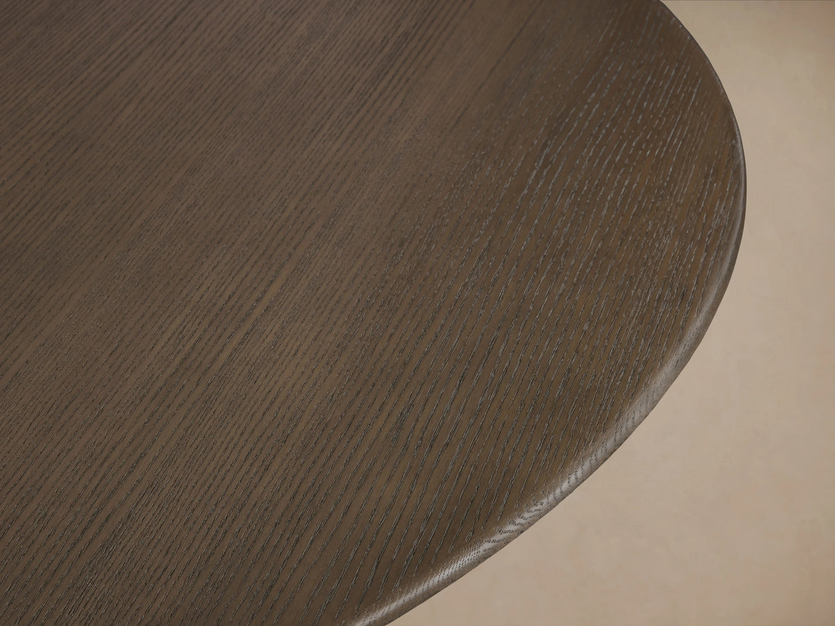 Saint Germain Round Wood Dining Table with dark oak top and elegant gold-toned steel launette base, on wooden floor.