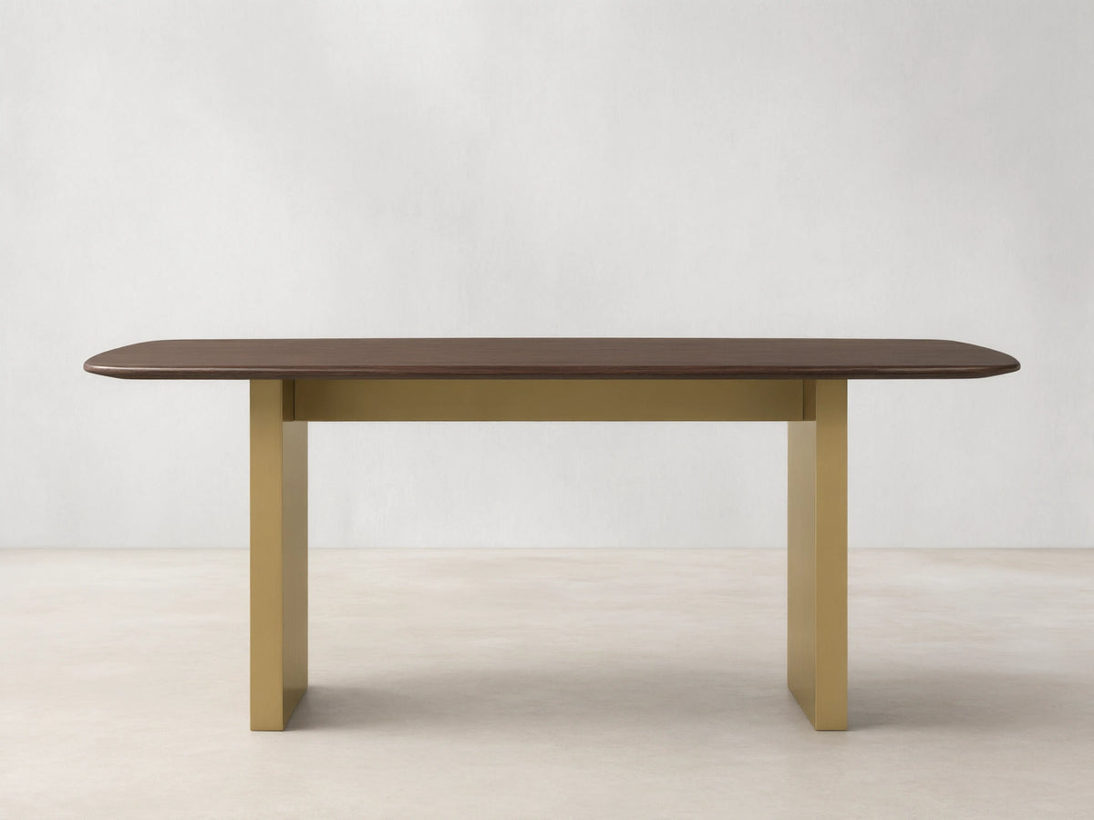 Wood dining table with a solid oak top in dark finish, supported by a rectangular base in antique brass. Placed on a wooden floor.